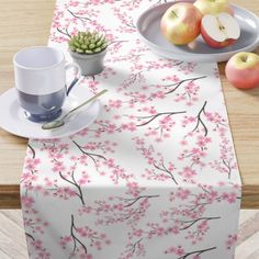 a table topped with plates and cups next to an apple tree covered in pink flowers