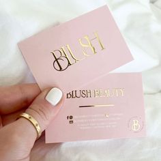 two pink business cards with gold foil lettering on the front and back, one being held by a woman's hand