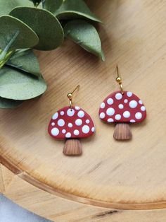 red and white mushroom shaped earrings sitting on top of a wooden table