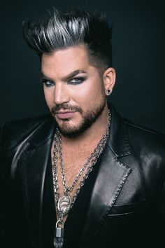 a man with black hair and piercings on his head wearing a leather jacket, chain necklace and earrings