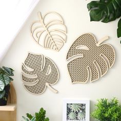 three wooden cutout leaves on a wall next to potted plants