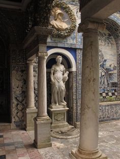 a statue in the middle of a room with columns and tile work on the walls