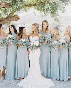 a group of women standing next to each other holding bouquets in front of a tree