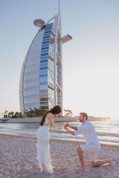 a man kneeling next to a woman on top of a sandy beach