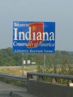 a welcome sign for indiana crossroads of america on the side of a highway with trees in the background