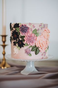 a pink cake with flowers on it sitting on a table next to a candle and some candlesticks