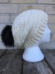 a white knitted hat with black fur pom - pom in front of a brick wall