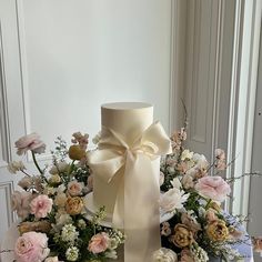 a white cake sitting on top of a table covered in flowers and ribbon tied around it