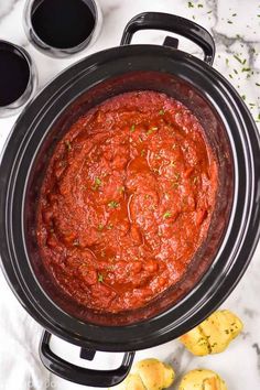 a slow cooker filled with marinara sauce next to some garlic and lemons