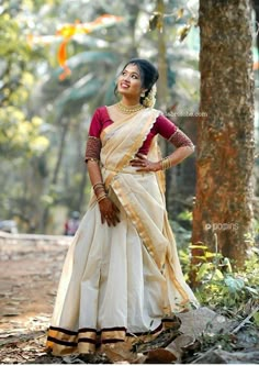 a woman standing in the woods wearing a white and red sari