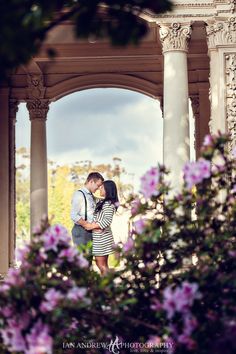 a man and woman standing in front of a gazebo with purple flowers on the ground