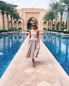 a woman is standing in front of a pool wearing sunglasses and a strapless dress