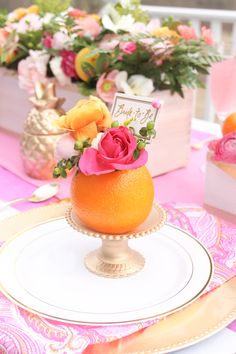 there is an orange on the table with flowers in it and a place setting for two