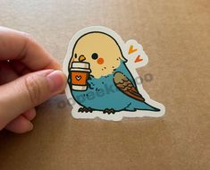 a hand holding a sticker with a bird on it and a cup in its beak