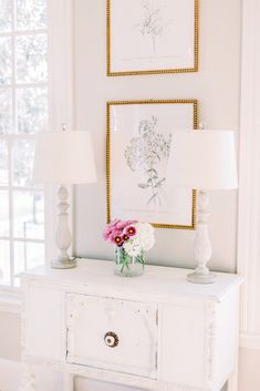 a white dresser with flowers and pictures on the wall