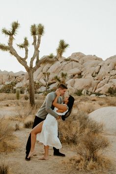 a man and woman kissing in the desert with joshua tree behind them, while holding each other's leg