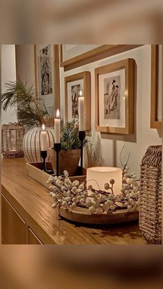 a wooden table topped with lots of candles next to pictures and vases filled with plants