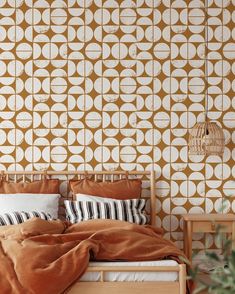 a bed with an orange comforter in front of a wallpapered bedroom area