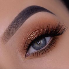 a woman's eye with gold glitters on her lashes and brown eyeshadp