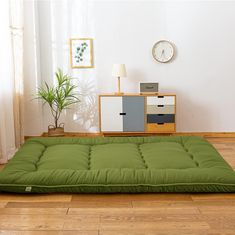 a green mattress on the floor in front of a white wall with a clock above it