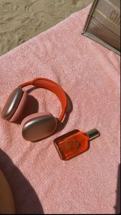 an orange headphones laying on top of a pink towel next to a brown bottle