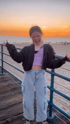 a young woman standing on top of a wooden pier next to the ocean at sunset