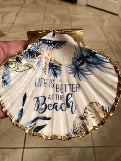 a hand holding a seashell with the words life is better at the beach on it