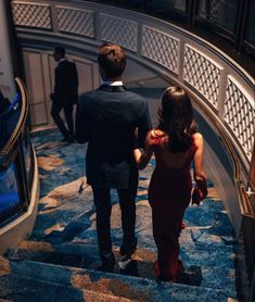 a man and woman walking down an escalator in a building with blue carpet