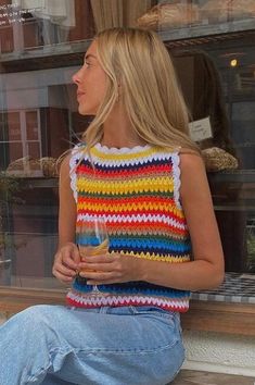 a woman sitting on a window sill with a glass in her hand and looking out the window