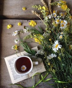 a cup of coffee sitting on top of an open book next to wildflowers