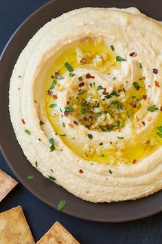 an image of hummus with olives and herbs on top in a plate next to crackers