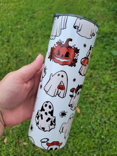 a person holding a white cup with halloween pictures on it in their hand and green grass behind them