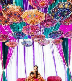 two women sitting on a red couch in front of colorful umbrellas hanging from the ceiling