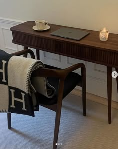 a laptop computer sitting on top of a wooden desk next to a chair with a blanket