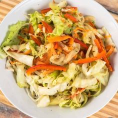 a white bowl filled with lettuce, carrots and coleslaw on top of a wooden cutting board