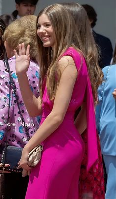 a woman in a pink dress waves to the crowd