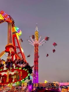 the carnival rides are brightly lit up at night, with people riding on them and flying kites in the air