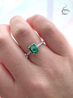 a woman's hand holding an emerald and diamond ring