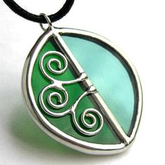 a green glass pendant with two spirals on it's side and a black cord