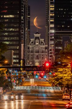 a city street at night with the moon in the sky and cars driving on it