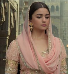 a woman in a pink outfit with gold jewelry on her head and wearing a shawl