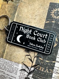 a black keychain with the words night court book club on it sitting on top of a piece of newspaper