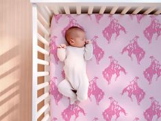 a baby is sleeping in a crib with pink horses on the wall behind it