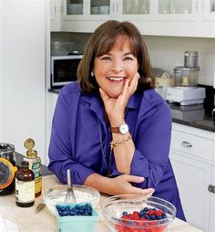 a woman sitting at a kitchen counter in front of bowls of berries and blueberries