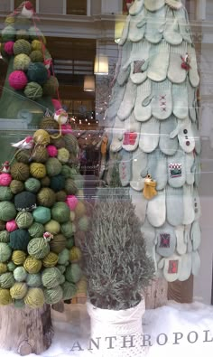 two knitted christmas trees in front of a store window with balls of yarn hanging from them