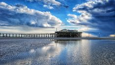 the clouds are reflected in the water near a pier and building on the beach with it's reflection