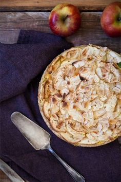 an apple pie on a wooden table next to two apples