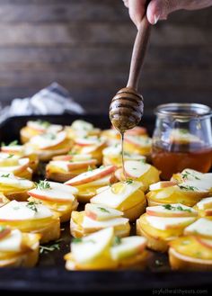 a person is spooning honey over some apples on a pan with other food items