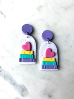 two heart shaped earrings on top of a marble counter with purple, yellow and green accents