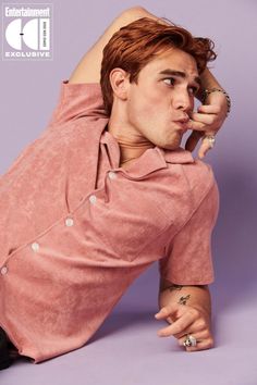 a young man laying on the ground wearing a pink shirt and black pants with his hands behind his head